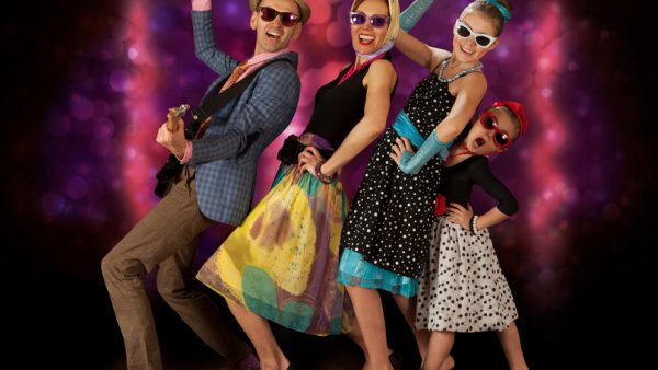 Rockabilly family band having fun posing with guitar and vintage microphone in 1950’s style clothing.